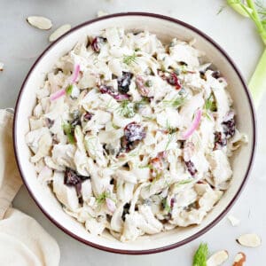 Chicken fennel salad in a serving bowl surrounded by ingredients and a napkin.