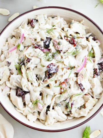 Chicken fennel salad in a serving bowl surrounded by ingredients and a napkin.