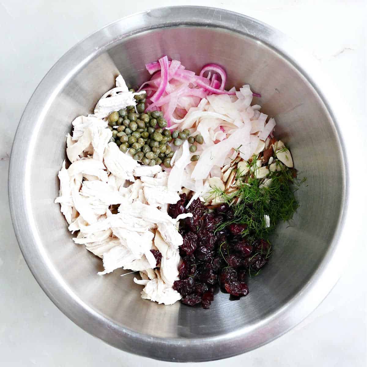 Chicken, capers, fennel, onion, dried cherries, and almonds in a bowl.