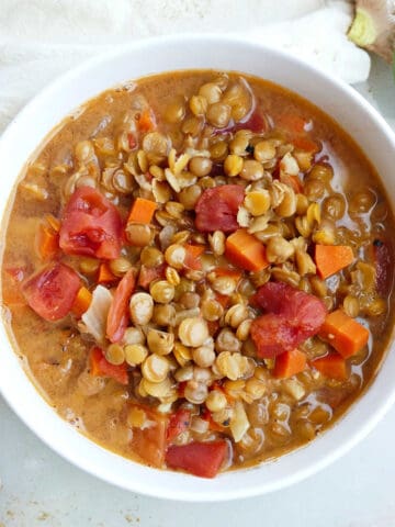 Bowl of coconut lentil soup next to ingredients, napkin, and spoon.