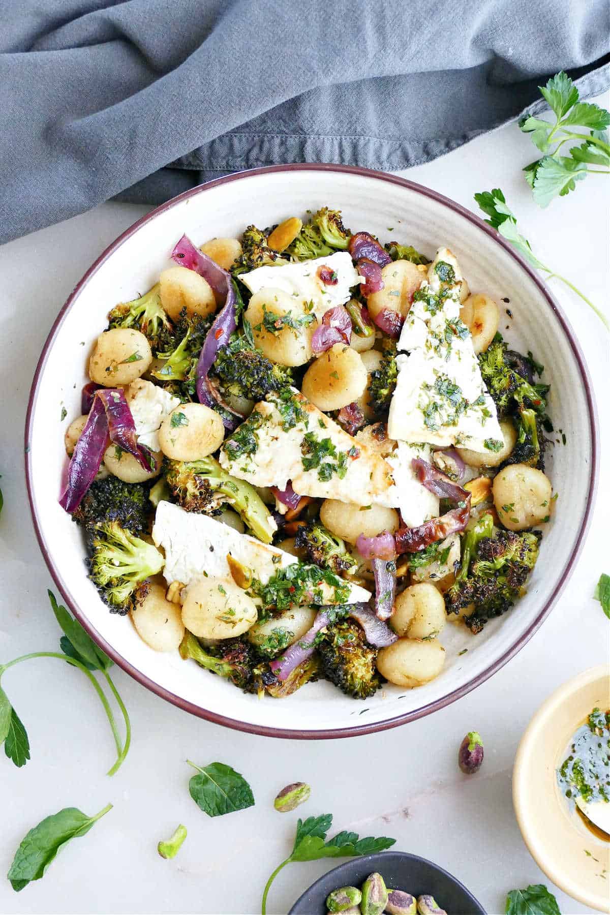 Gnocchi with feta dinner in a bowl next to herbs, ingredients, and a napkin.