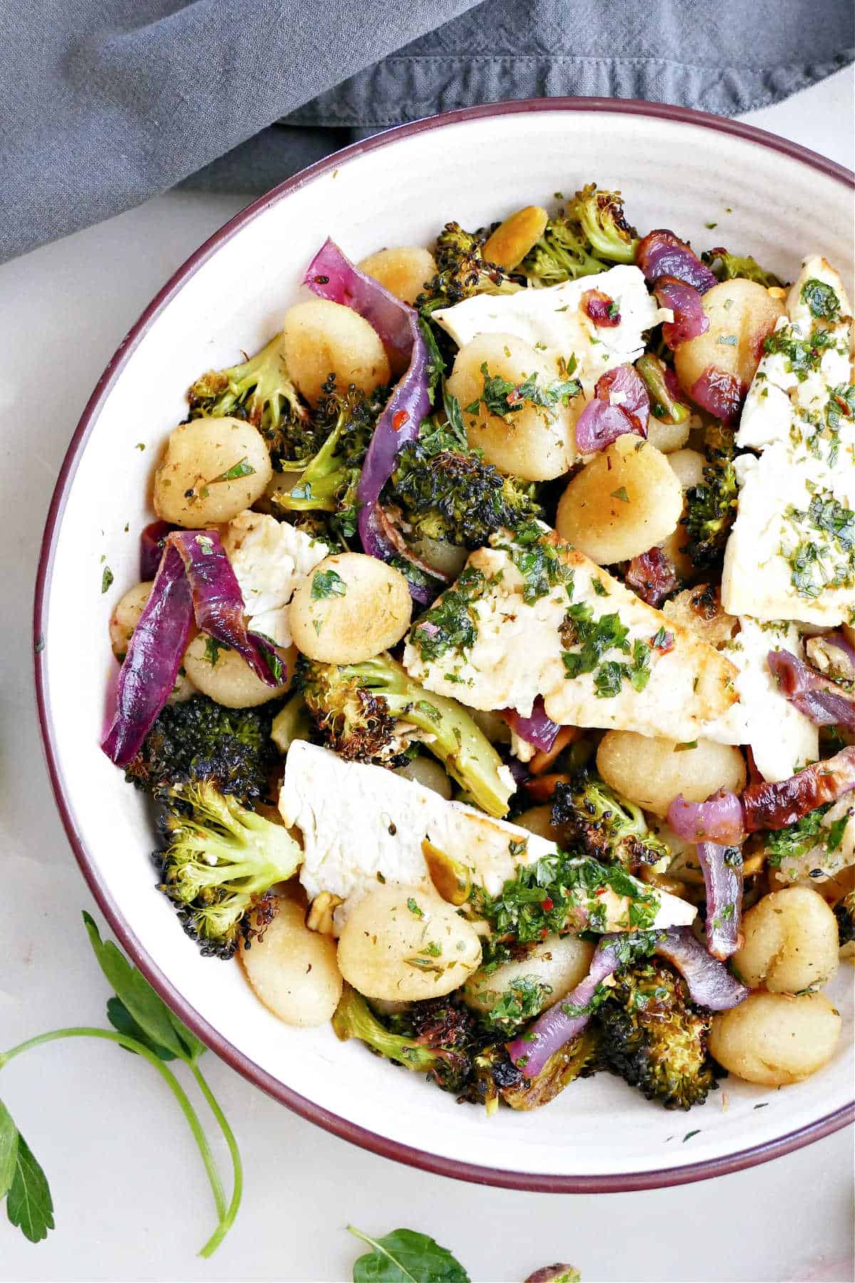 Gnocchi, feta, vegetables, and herb sauce in a bowl next to a napkin.