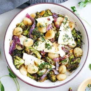 Gnocchi with feta dinner in a bowl next to herbs, ingredients, and a napkin.