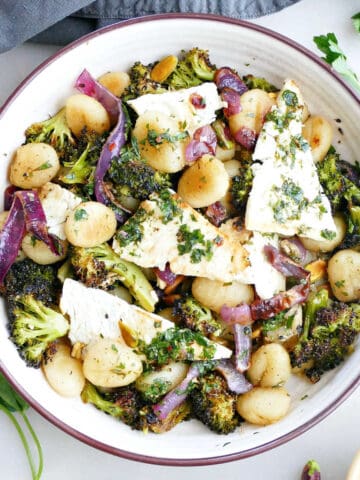 Gnocchi with feta dinner in a bowl next to herbs, ingredients, and a napkin.