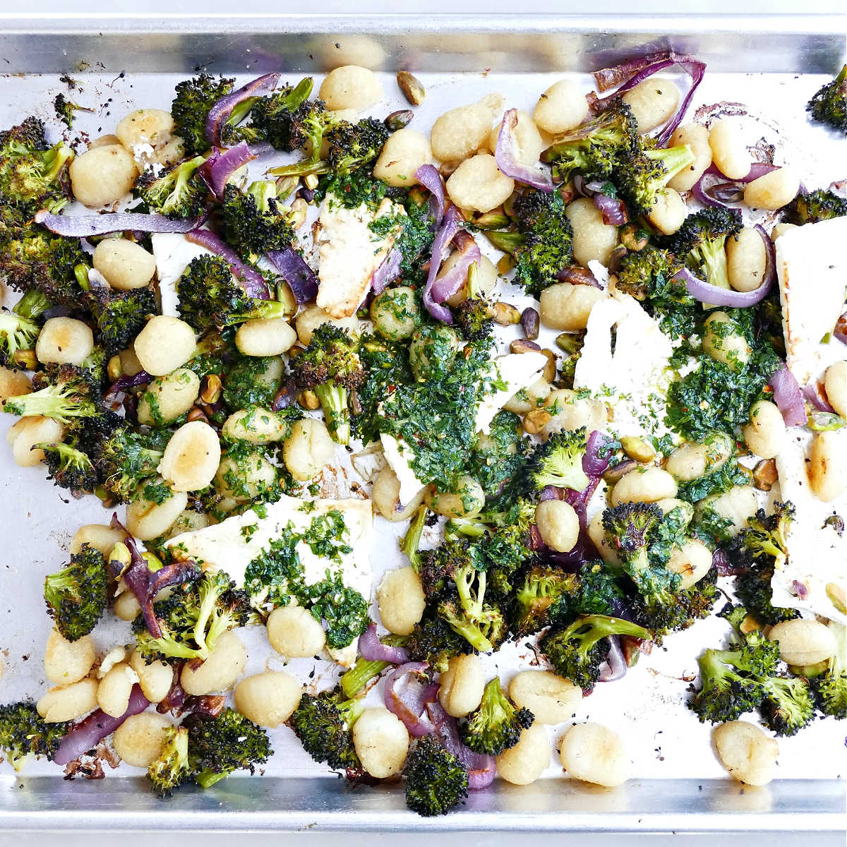 Gnocchi and feta dinner tossed with herb sauce on a baking sheet.