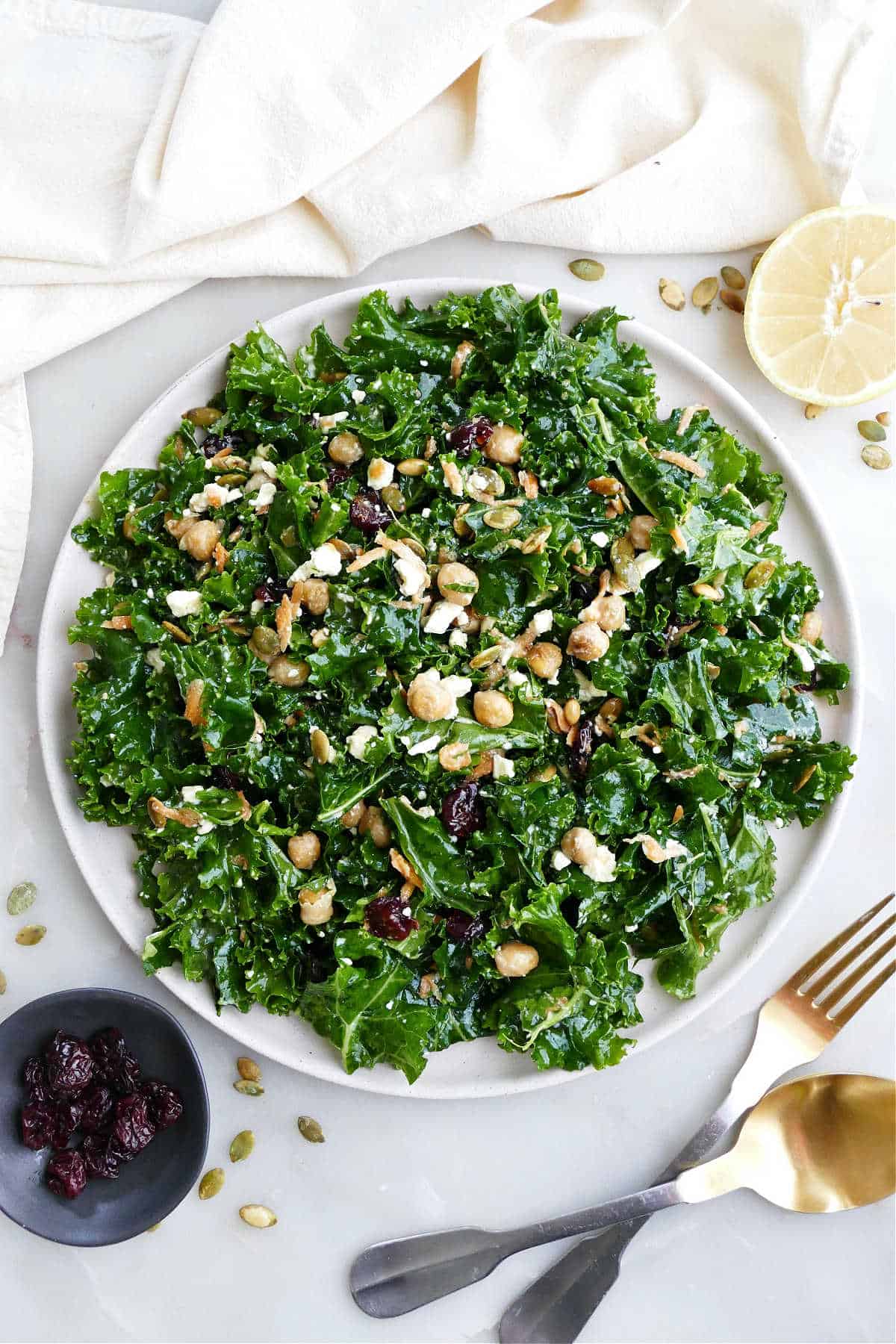 Kale salad on a serving plate next to ingredients, a napkin, and utensils.