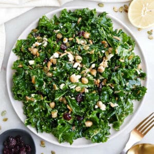 Kale salad on a serving plate next to ingredients, a napkin, and utensils.