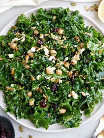 Kale salad on a serving plate next to ingredients, a napkin, and utensils.