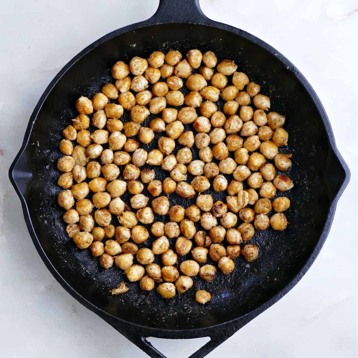 Chickpeas cooking in olive oil and seasonings in a skillet.