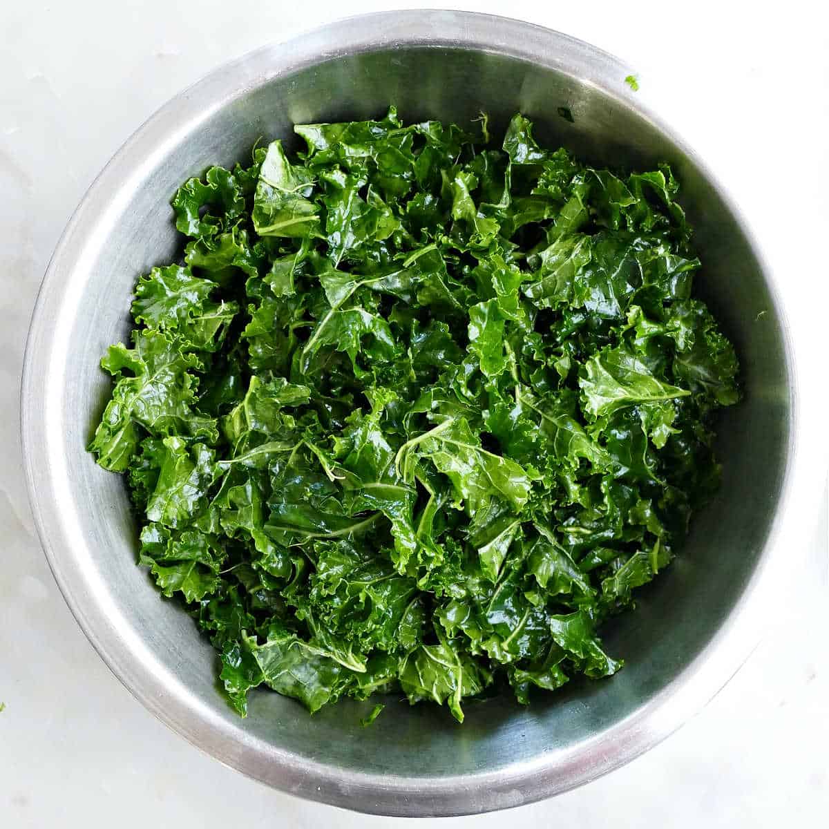 Kale massaged with olive oil in a large bowl.