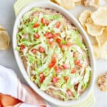Taco bean dip in a serving dish with lettuce and tomatoes.
