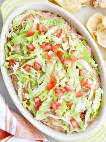 Taco bean dip in a serving dish with lettuce and tomatoes.