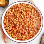 Baked beans in a serving bowl on a counter next to a spoon and napkin.
