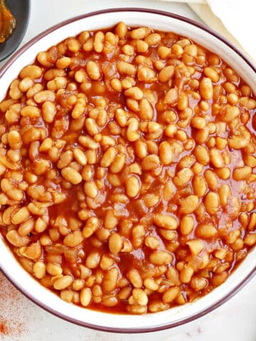 Baked beans in a serving bowl on a counter next to a spoon and napkin.