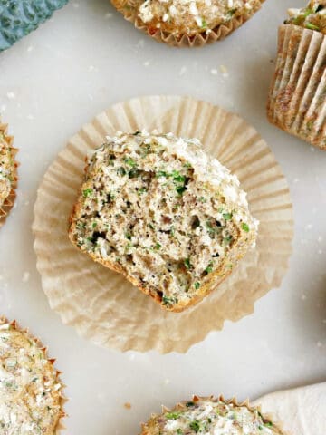 Half of a kale cottage cheese muffin cut side up on a liner next to other muffins.