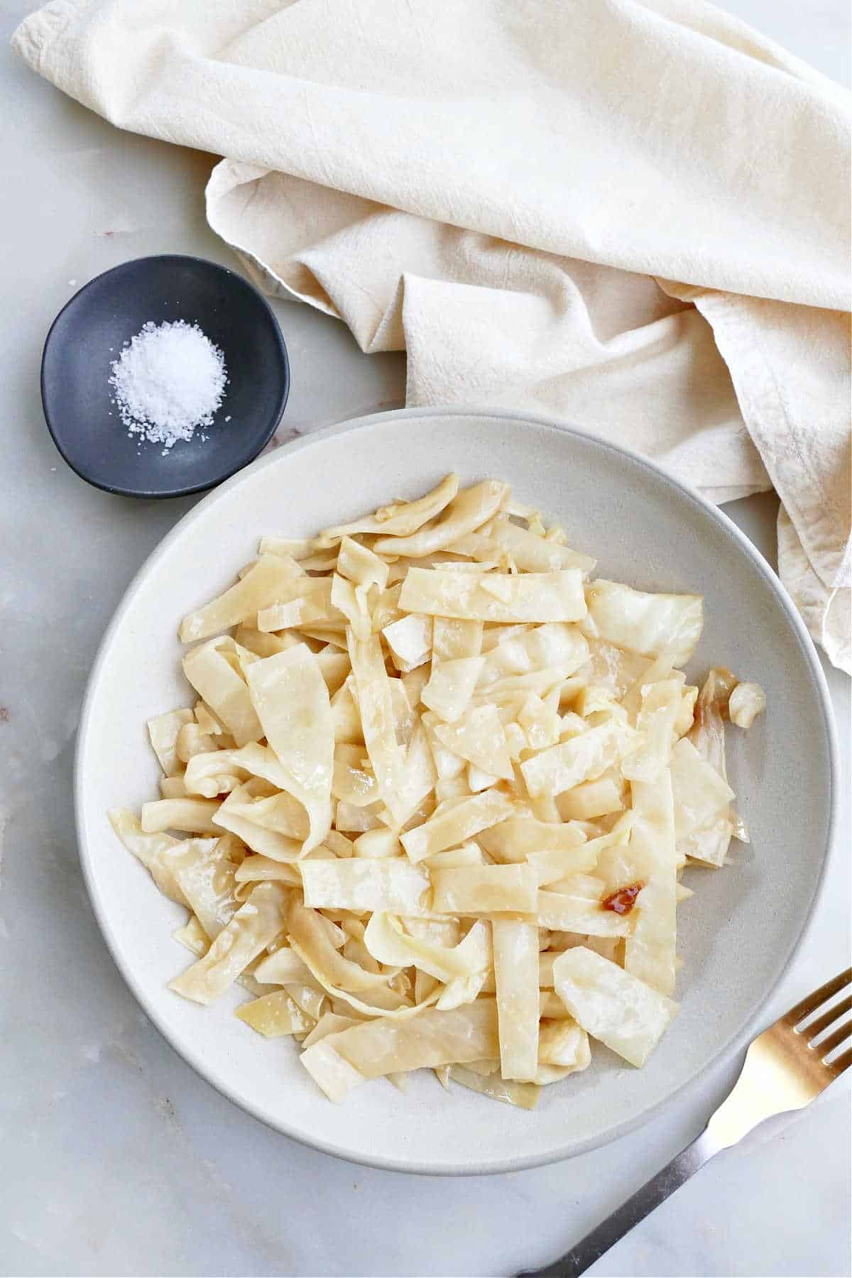 Slow cooker cabbage on a plate next to fork, napkin, and bowl of salt.