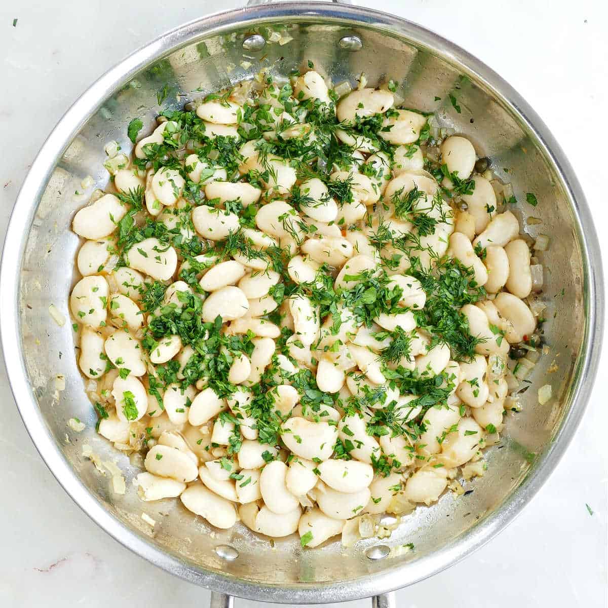 Butter beans cooking in a skillet with fresh herbs.