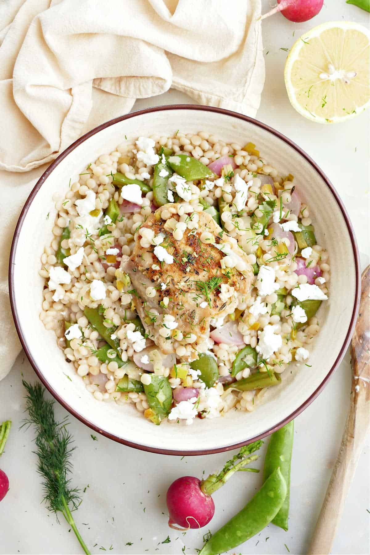 Bowl with couscous and vegetables topped with chicken and goat cheese.