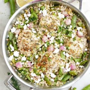 Large skillet with chicken thighs, couscous, and vegetables next to ingredients.