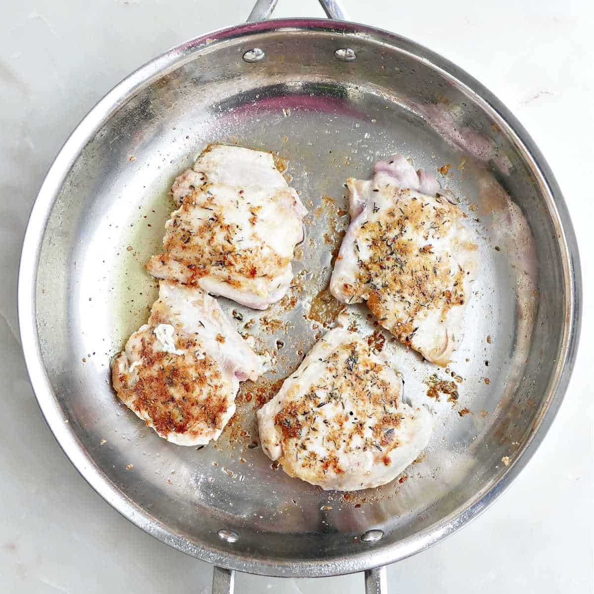 Seasoned chicken thighs cooking in oil in a skillet.