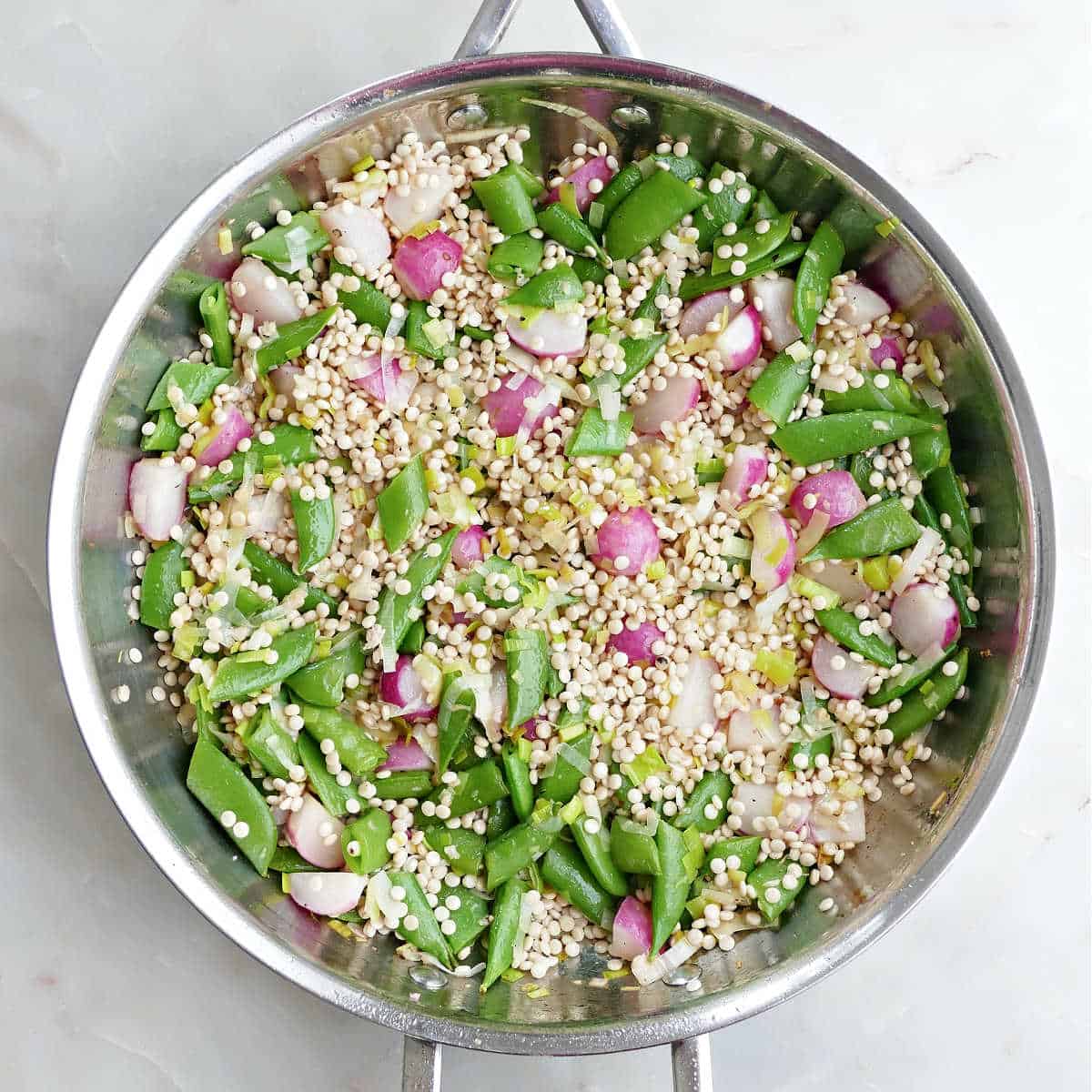 Spring vegetables and pearl couscous cooking in a skillet.
