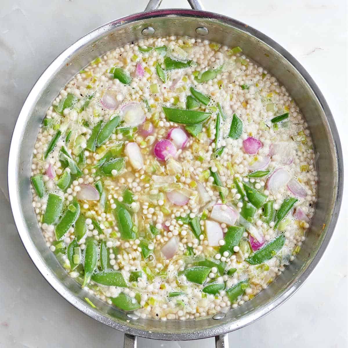 Couscous, radishes, snap peas, and chicken broth in a skillet.