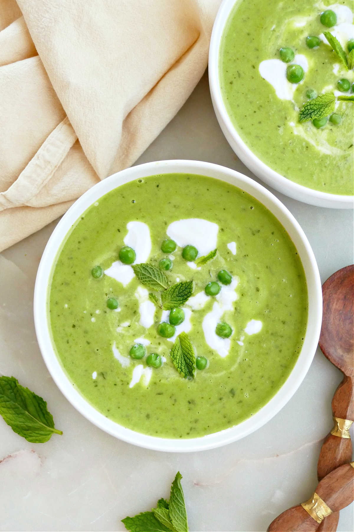 Bowls of pea and mint soup topped with peas and coconut yogurt on a counter.