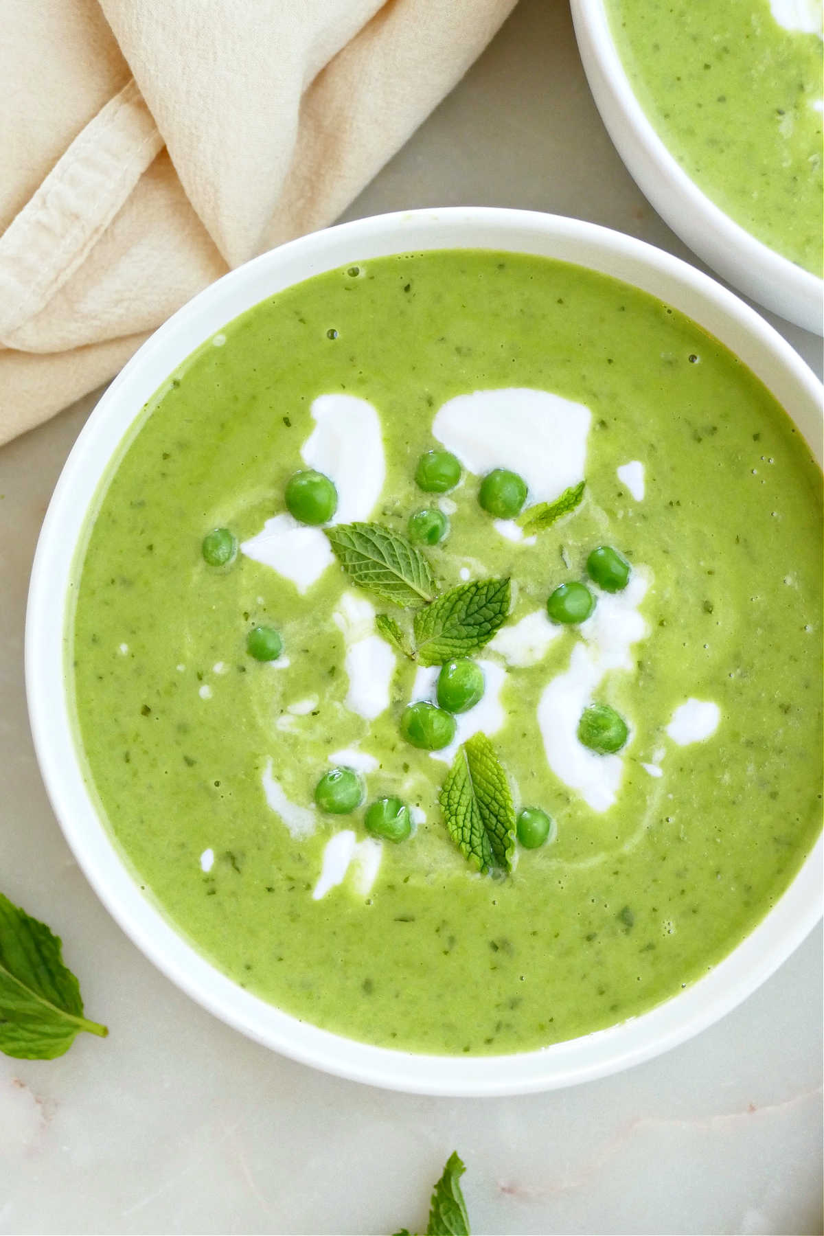 Minted pea soup in a bowl with garnishes next to a napkin.