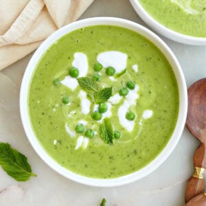 Mint leaves, peas, and coconut yogurt on top of pea and mint soup in a bowl.