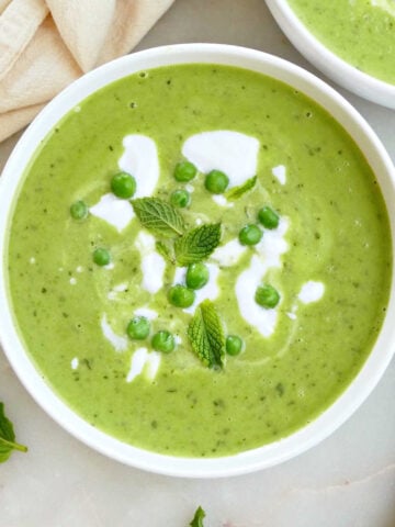 Mint leaves, peas, and coconut yogurt on top of pea and mint soup in a bowl.