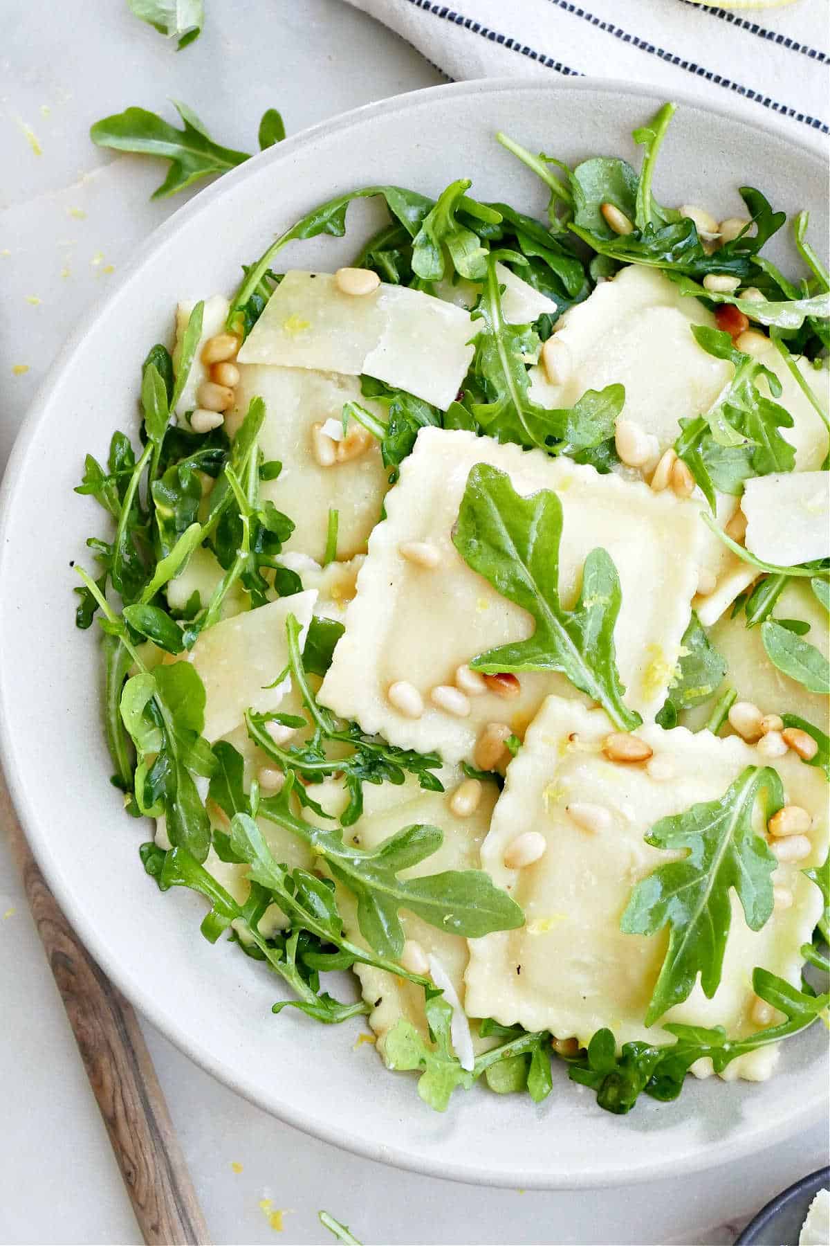 Ravioli salad with arugula, pine nuts, and parmesan in a bowl.