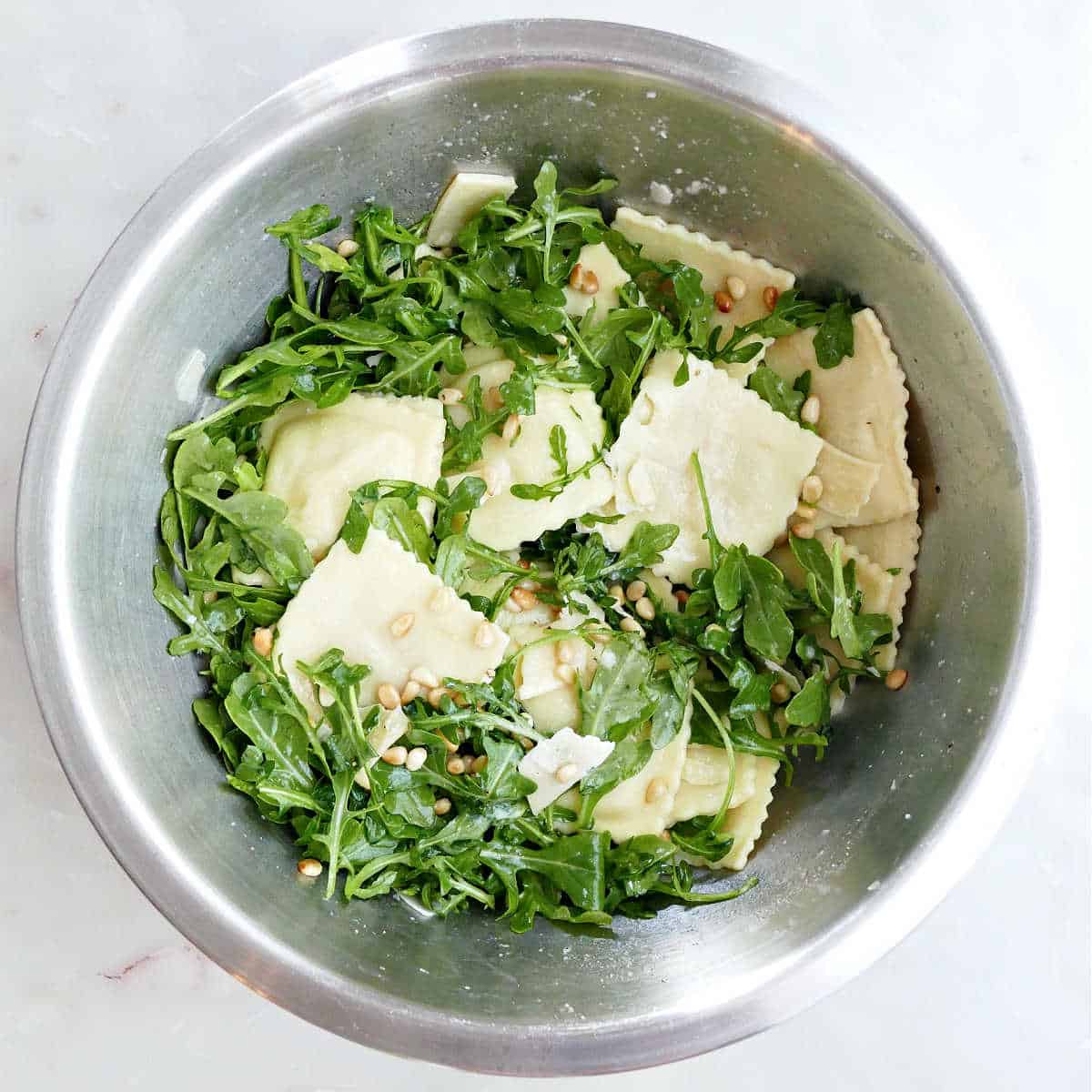 Ravioli pasta salad tossed in lemon dressing in a mixing bowl.