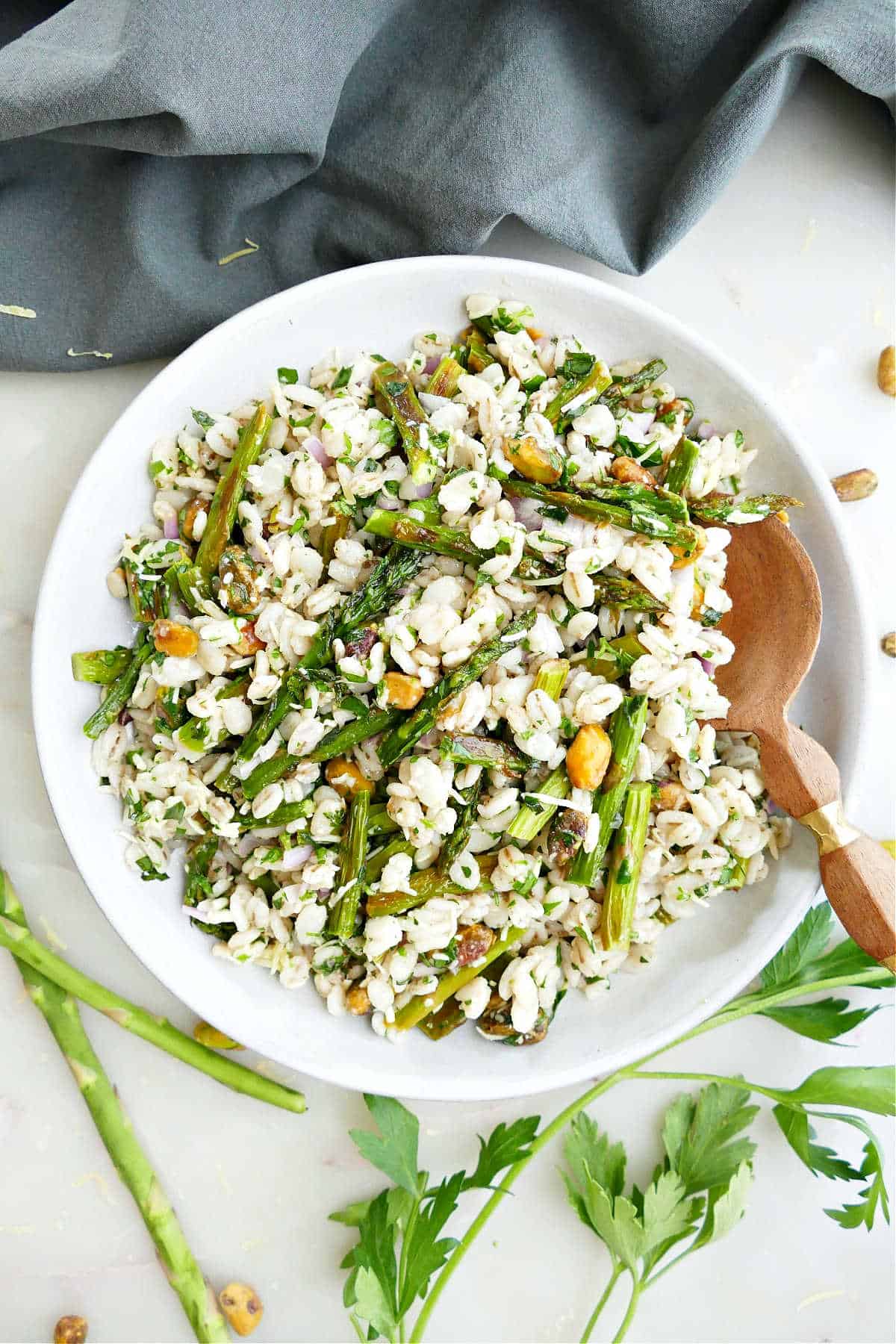 Roasted asparagus salad in a serving dish with a wooden spoon next to ingredients and a napkin.
