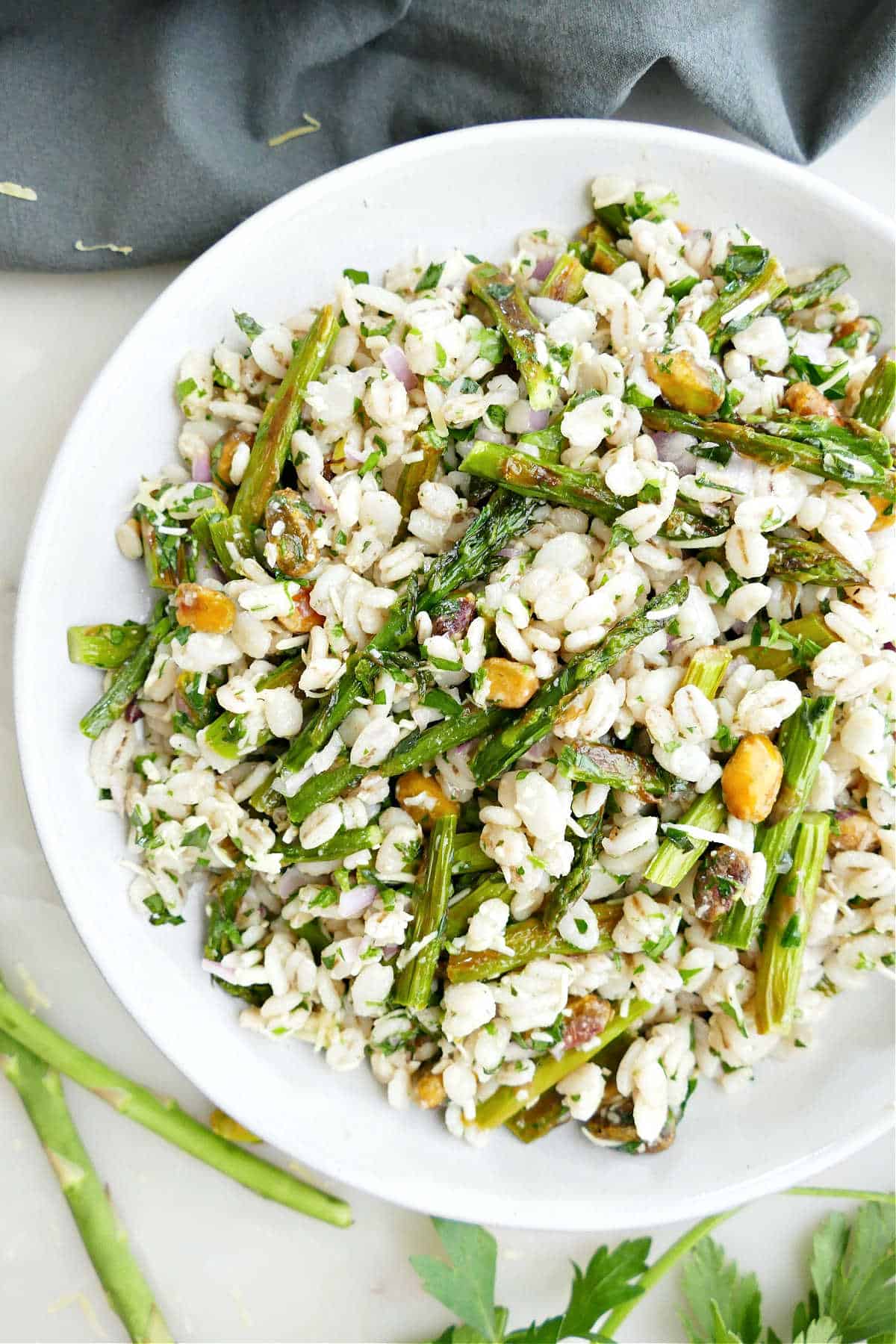 Asparagus and barley salad on a plate with pistachios and gouda cheese.