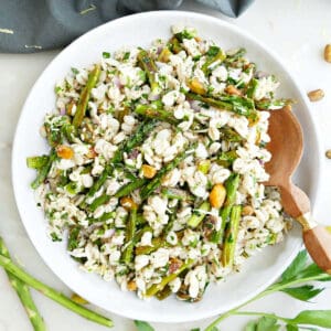 Roasted asparagus salad in a serving dish with a wooden spoon next to ingredients and a napkin.