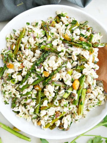 Roasted asparagus salad in a serving dish with a wooden spoon next to ingredients and a napkin.