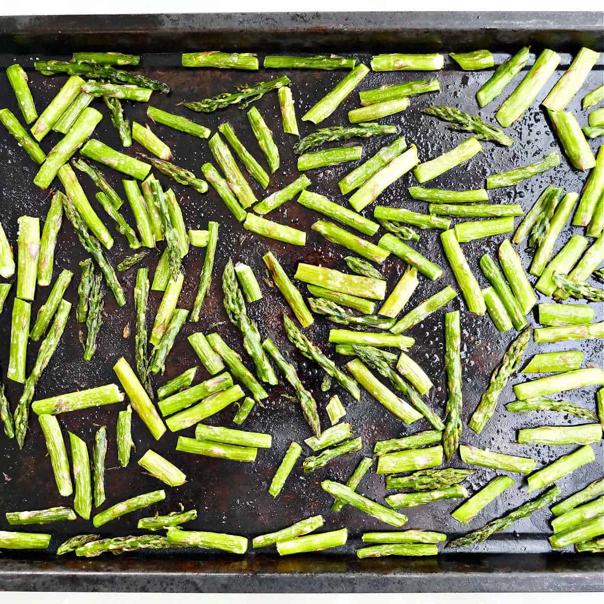 Pieces of asparagus on a baking sheet after roasting in the oven.