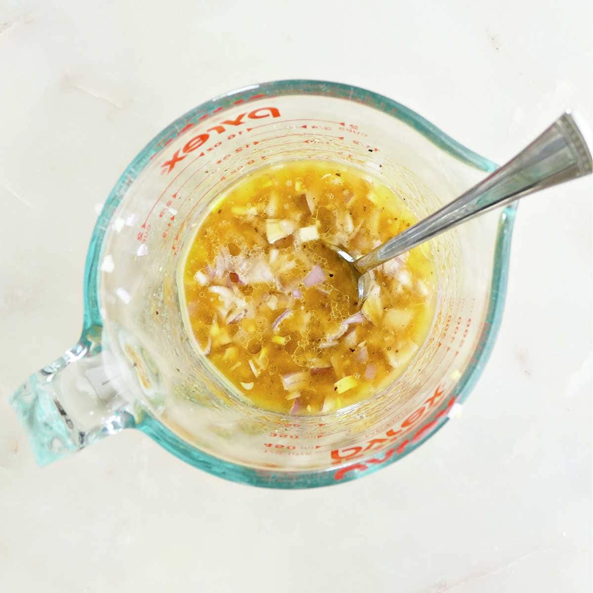 Shallots mixed together with olive oil, mustard, and lemon juice in a measuring cup.