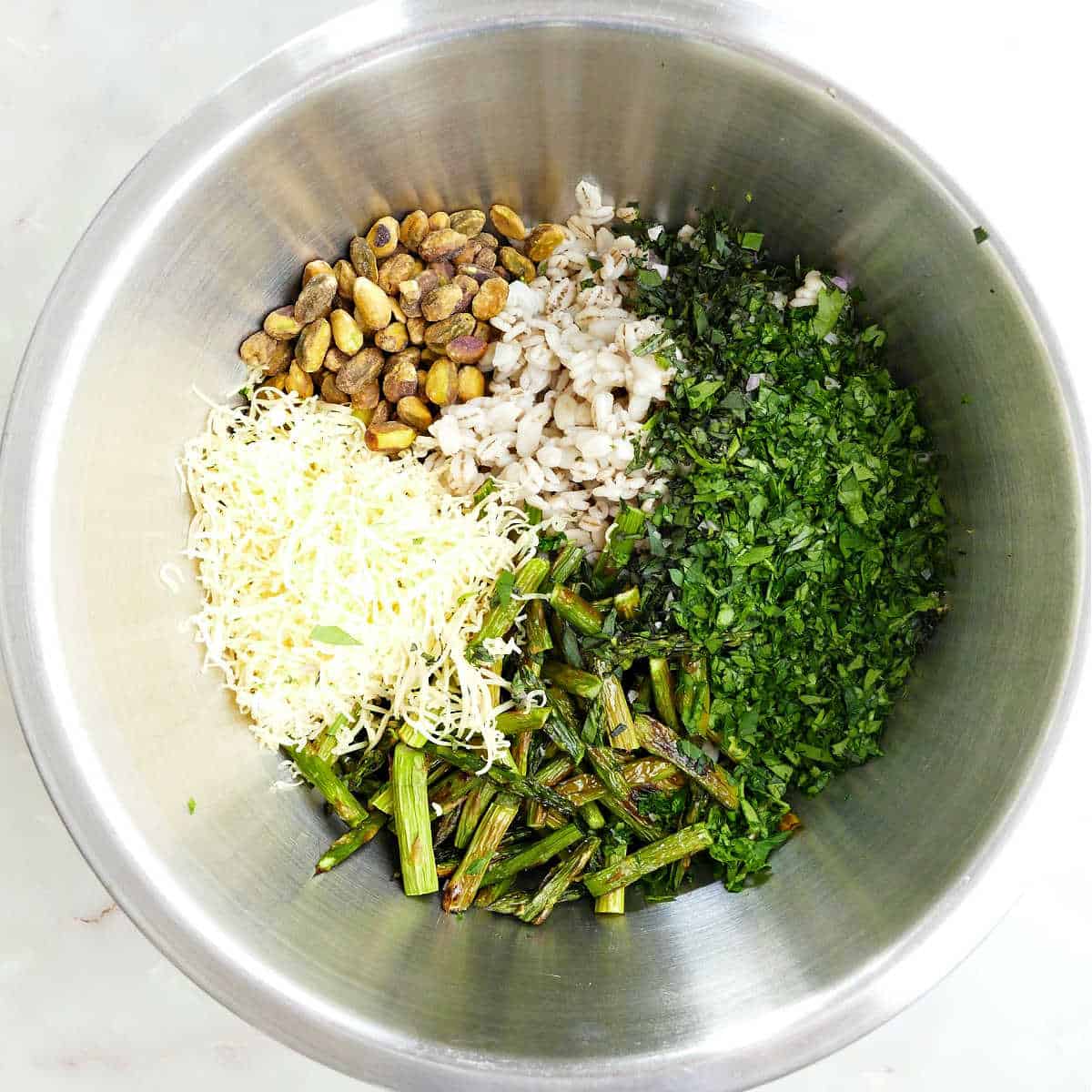 Gouda, pistachios, barley, fresh herbs, and roasted asparagus in a mixing bowl.