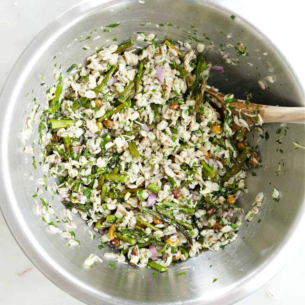 Roasted asparagus salad all mixed together in a bowl with a wooden spoon.