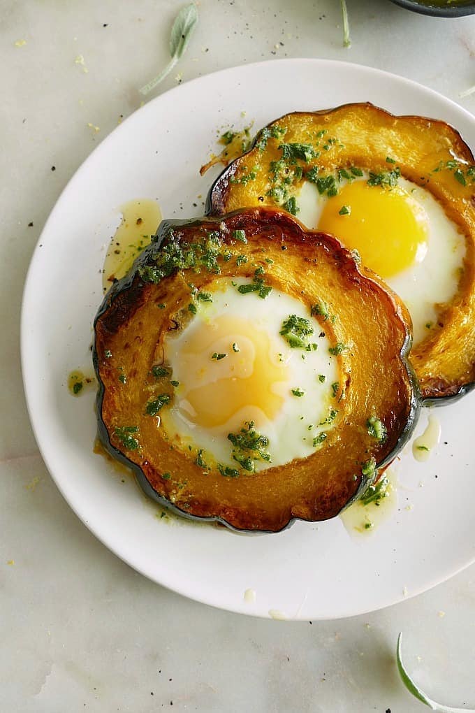 A plate of two acorn squash eggs-in-a-hole topped with sage brown butter on a white plate. 