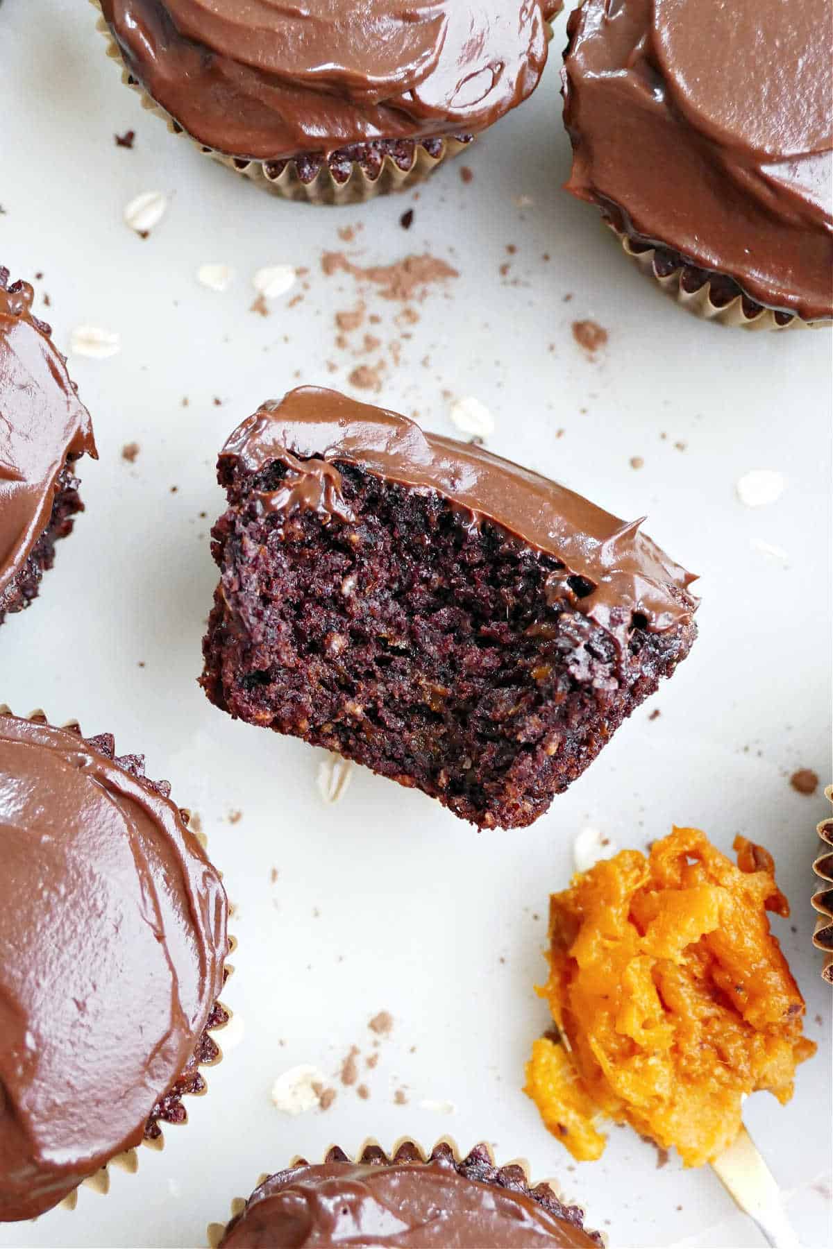 A close up of a frosted almond flour chocolate chip sweet potato cupcake with a bite taken out of it.