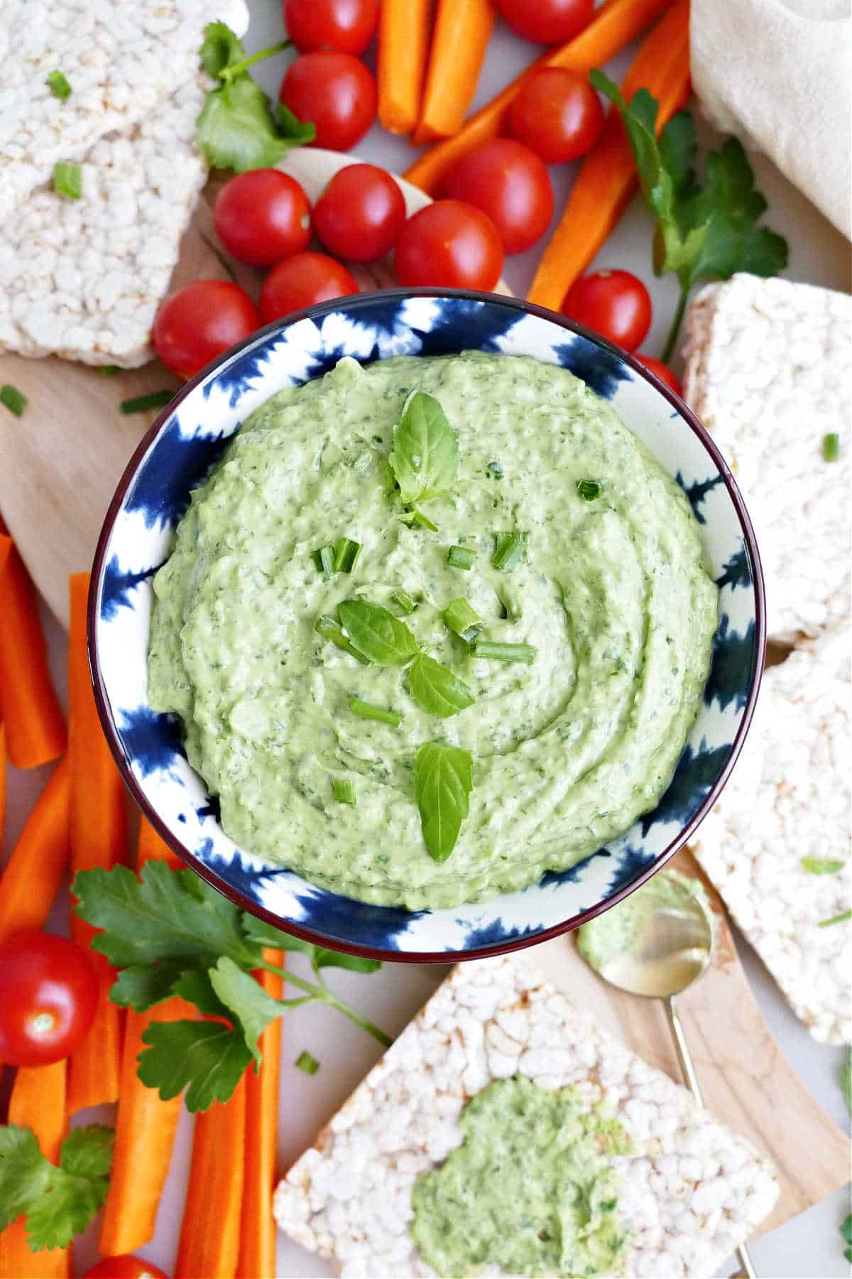 Green goddess dip made with avocado in a bowl surrounded by veggies and rice cakes.