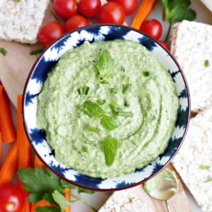 Green goddess dip made with avocado in a bowl surrounded by veggies and rice cakes.