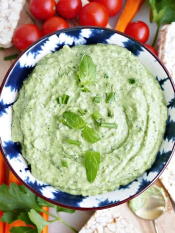 Green goddess dip made with avocado in a bowl surrounded by veggies and rice cakes.