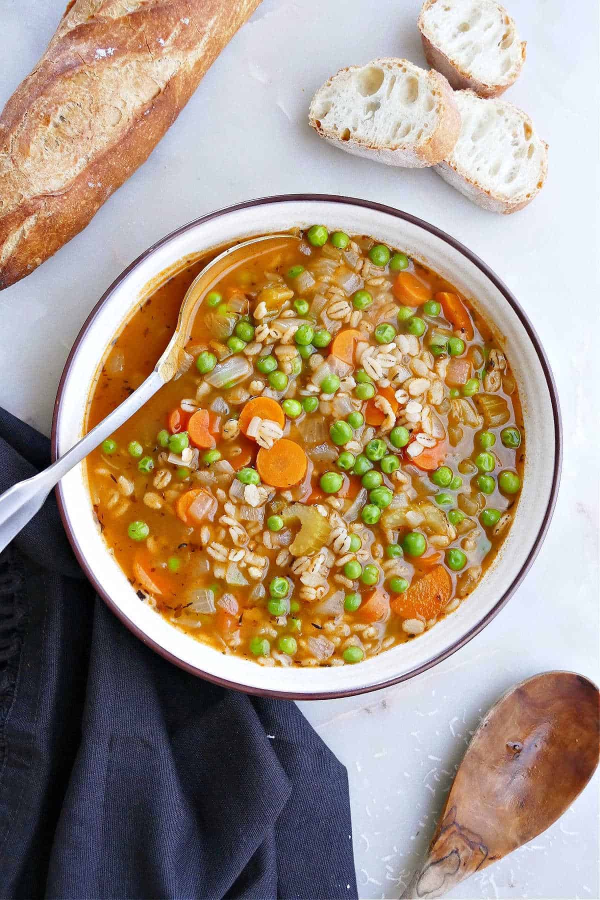 Veggie barley soup with spoon next to a loaf and slices of crusty bread.