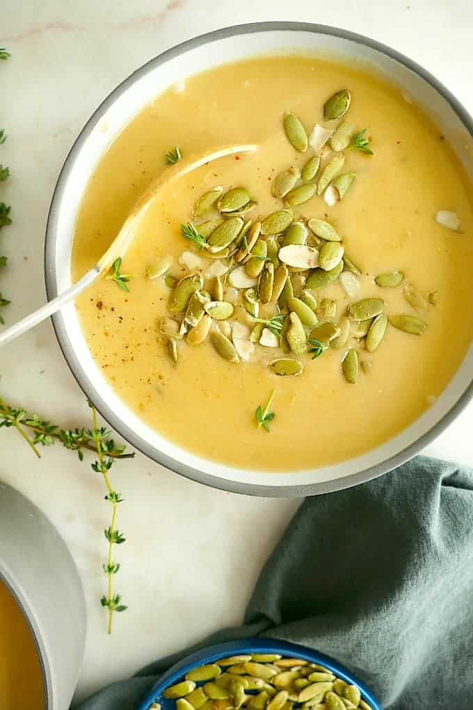 A bowl of vegan butternut squash and pear soup with a spoon in it topped with pepitas.