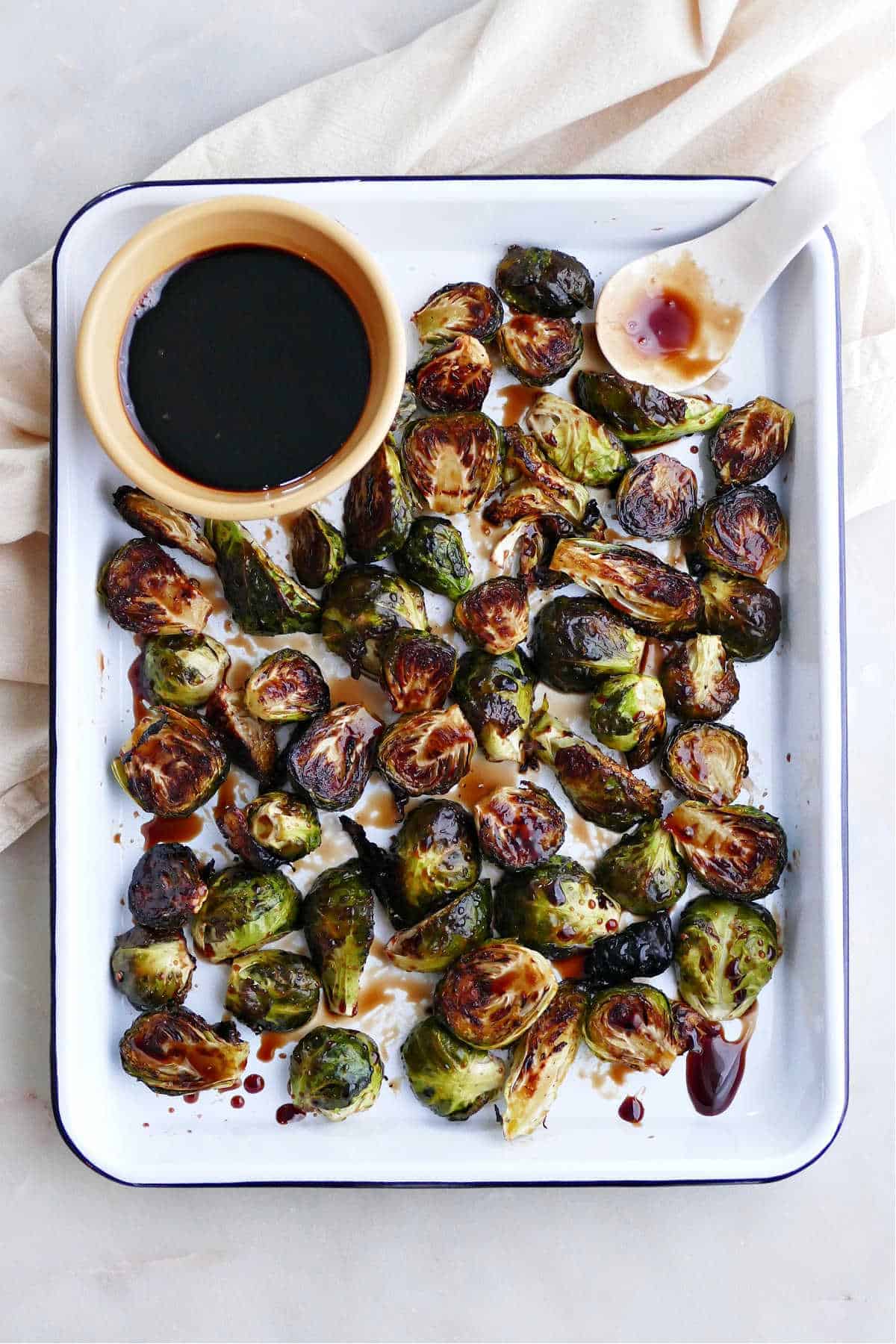 A large rectangle pan of Candied Brussels Sprouts with Maple Syrup in a bowl next to them.