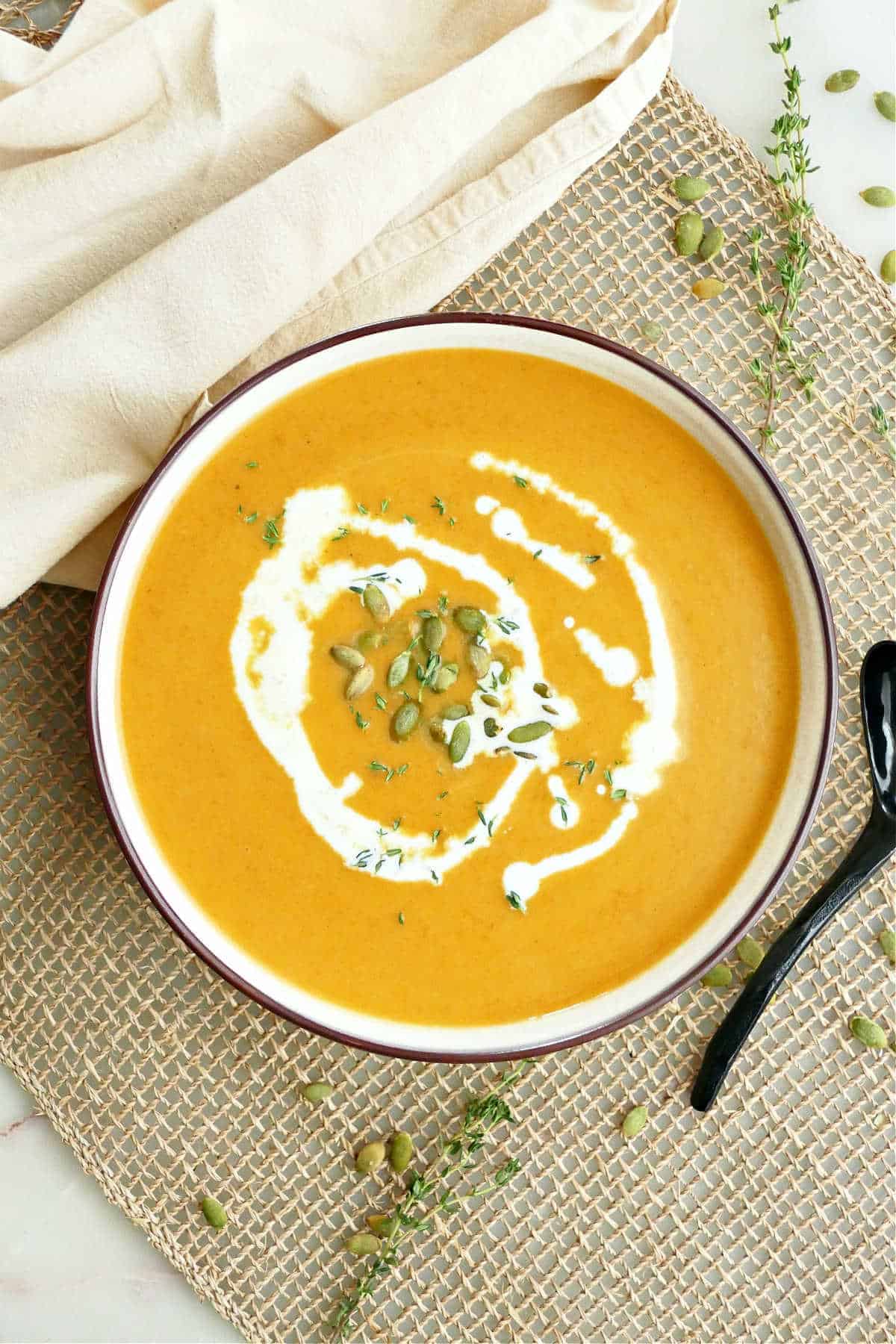 Carrot pumpkin soup on a placemat next to a napkin and spoon. 