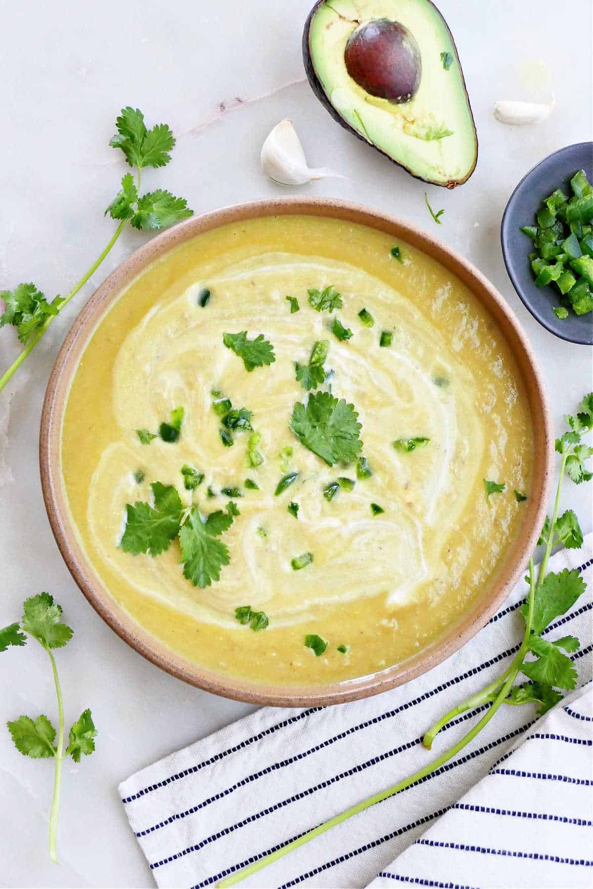 Cream of Jalapeño Soup next to an avocado and herbs.